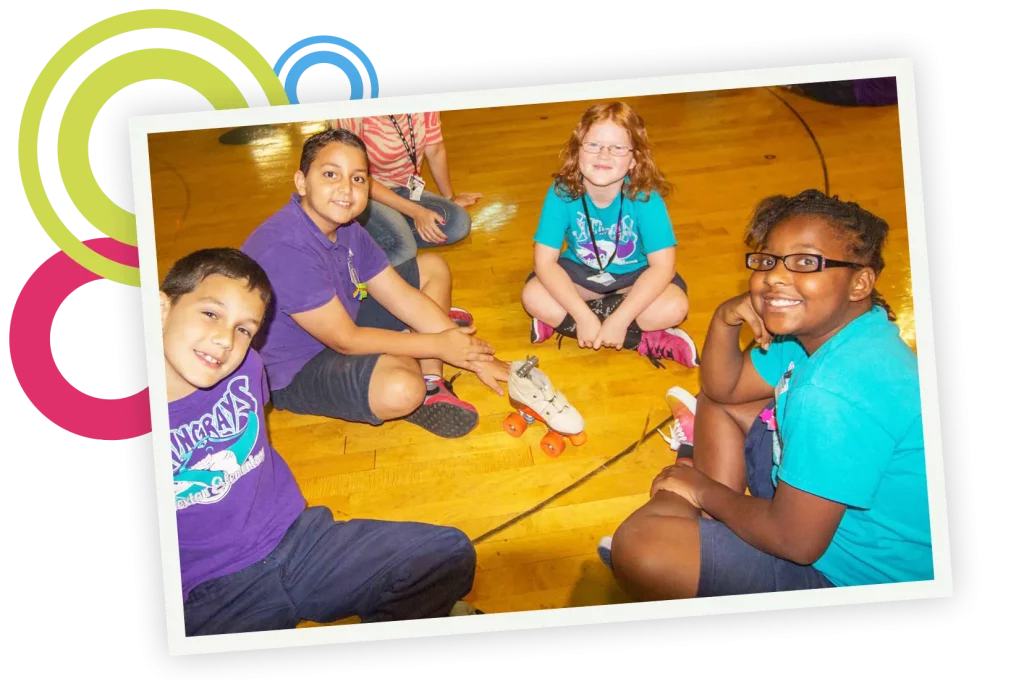 Groups of school kids sitting on the floor with a teacher playing with a roller skate