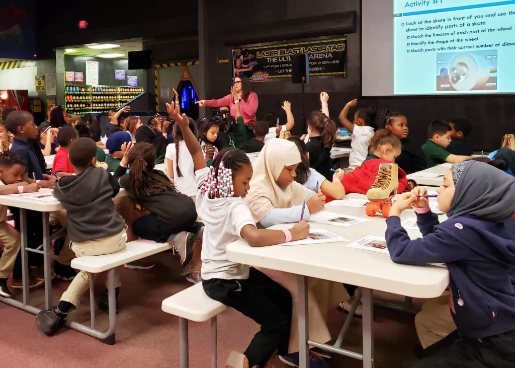 STEM teacher giving a lesson to a large field trip class at a roller skating rink